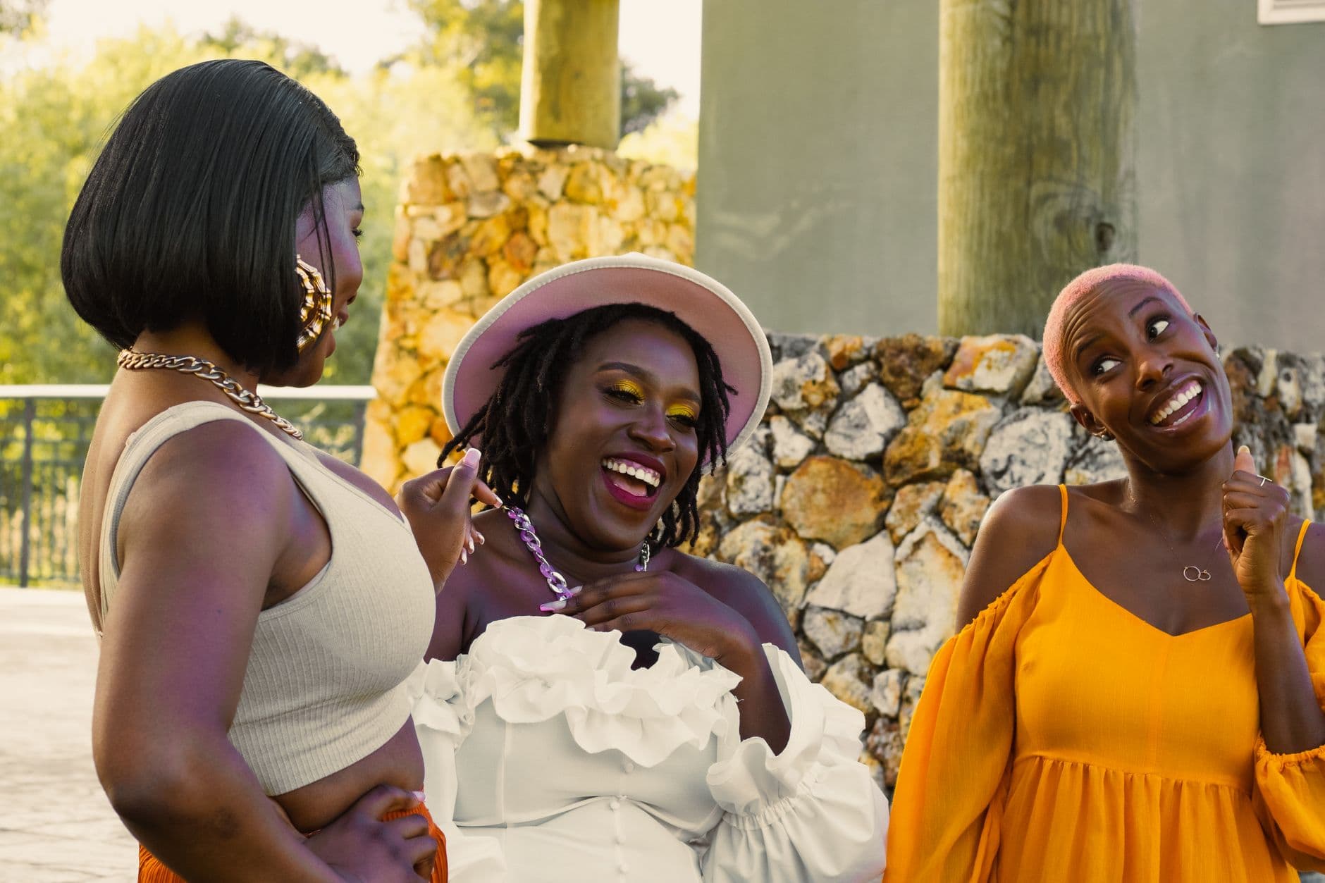 Three Black women laughing together outdoors in warm sunlight, the ease of being known by people who get it