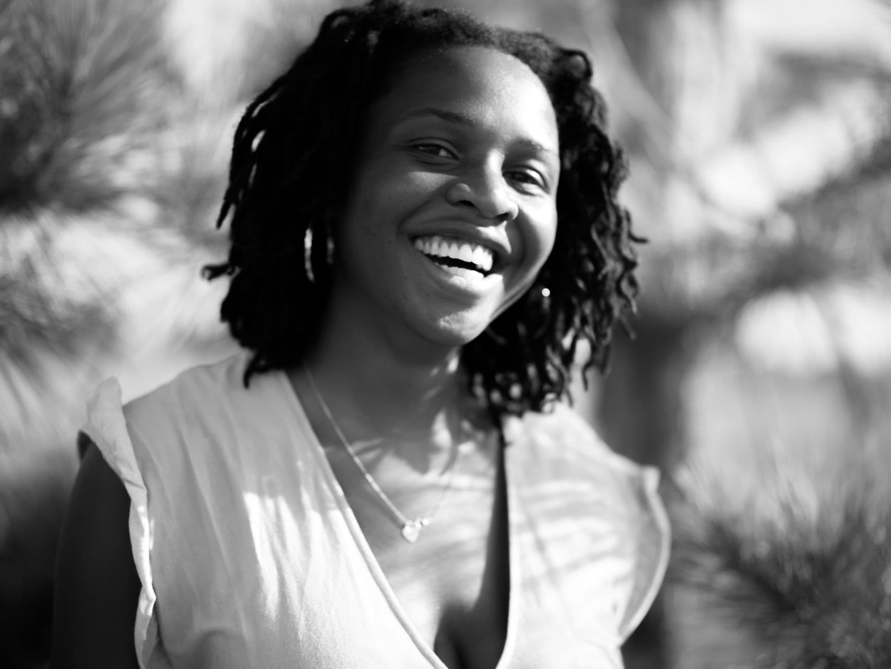 A Black woman laughing freely in sunlight, the joy of thriving rather than only surviving