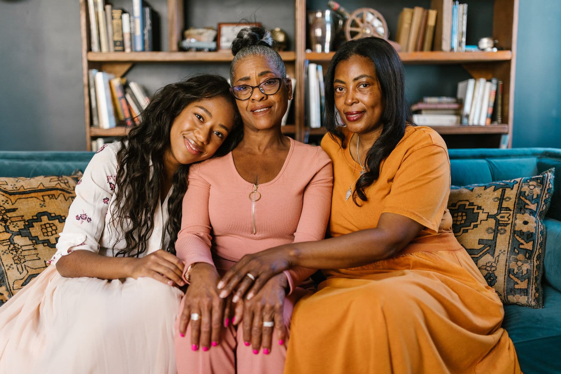 Three Black women of different generations sitting close together on a couch, leaning into each other